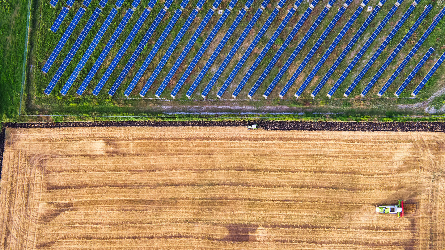 Overheard photo of a tractor ploughing a field, next to another field of solar panels