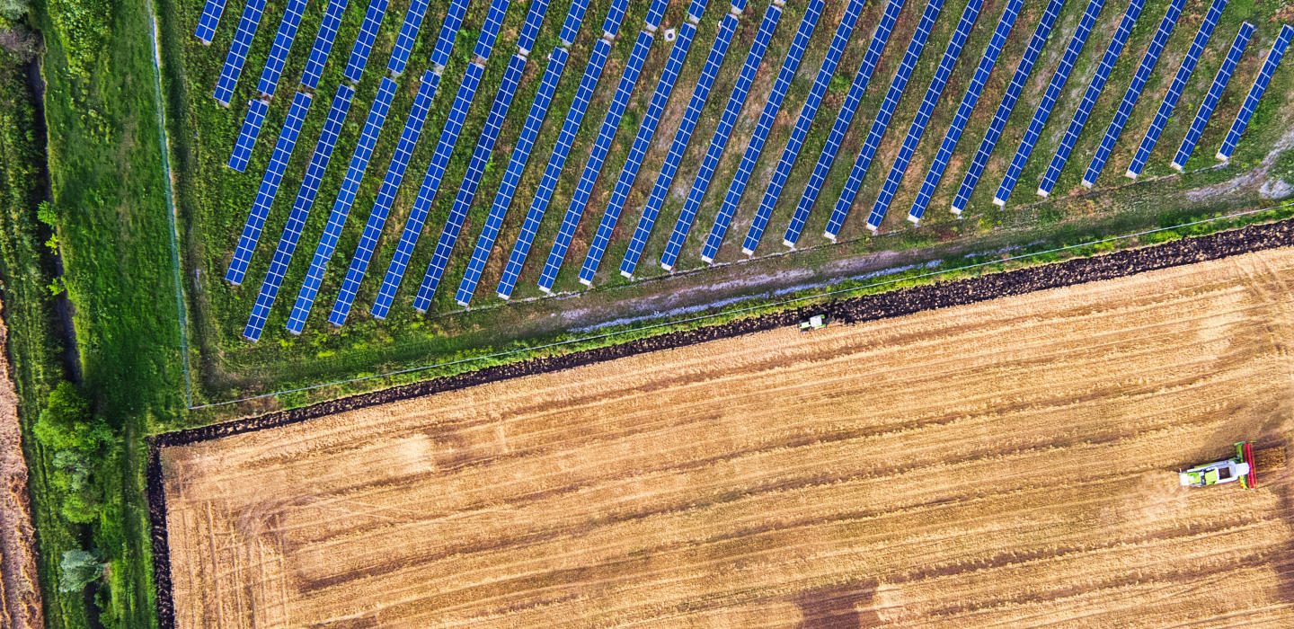Overheard photo of a tractor ploughing a field, next to another field of solar panels